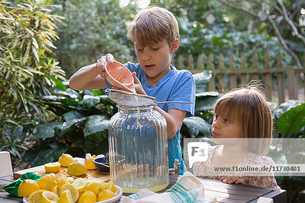 Junge und junge Schwester gießen Zitronensaft für Limonade am Gartentisch