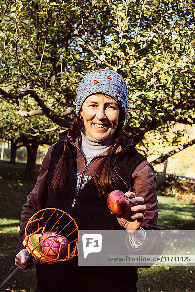 Portrait of woman holding fruit picker and fresh apple