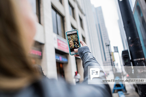 Junge Frau  im Freien  mit Smartphone in der Hand  bei Videoanruf  Rückansicht