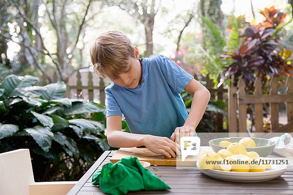 Junge quetscht Zitrone für Limonade am Gartentisch