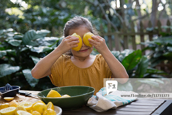 Mädchen hält Zitronen vor Augen  während sie am Gartentisch Limonade zubereitet