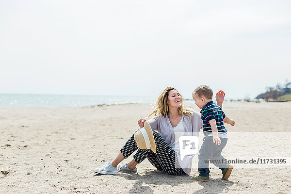 Junge Frau sitzt am Strand und spielt mit Kleinkind