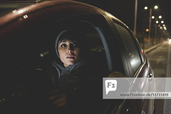 Frau  die nachts am Straßenrand der Stadt aus dem Autofenster schaut