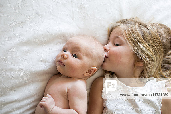 Draufsicht auf junges Mädchen und kleinen Bruder  die auf dem Bett liegen  Mädchen küsst kleinen Bruder