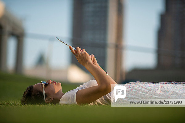 Mittelgroße erwachsene Frauen liegen im Park und verwenden ein digitales Tablett