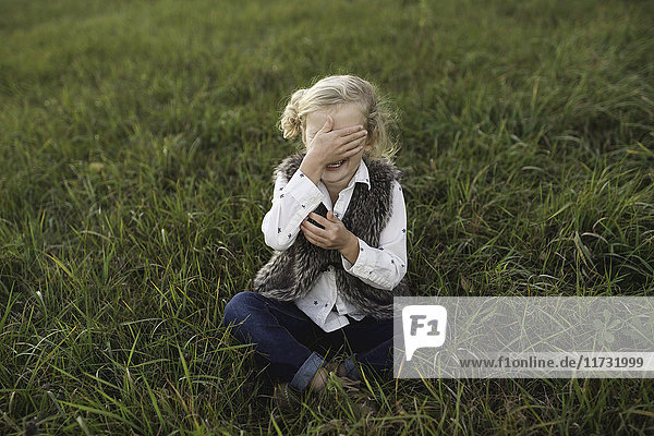 Junges Mädchen sitzt auf Gras und bedeckt die Augen