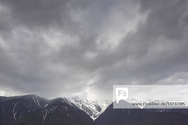 Dramatisch bewölkter Himmel und schneebedeckte Bergkette Bezirk Shangri-la Yunnan China