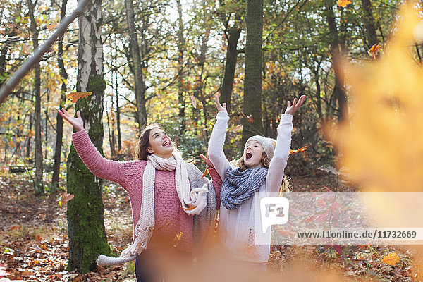Teenage girls in forest arms raised throwing autumn leaves smiling