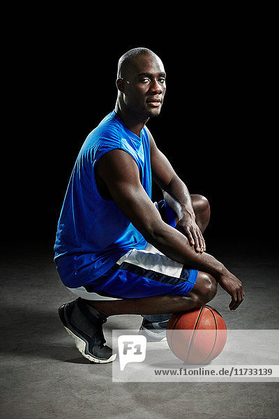 Studioporträt eines auf dem Ball knienden Basketballspielers
