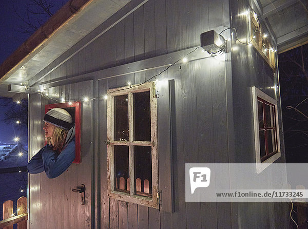 Reife Frau lehnt sich aus dem Fenster einer kleinen Holzhütte