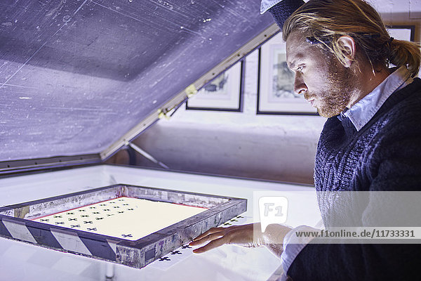 Junger Mann bereitet Bildschirm auf Leuchtkasten in traditioneller Druckwerkstatt vor