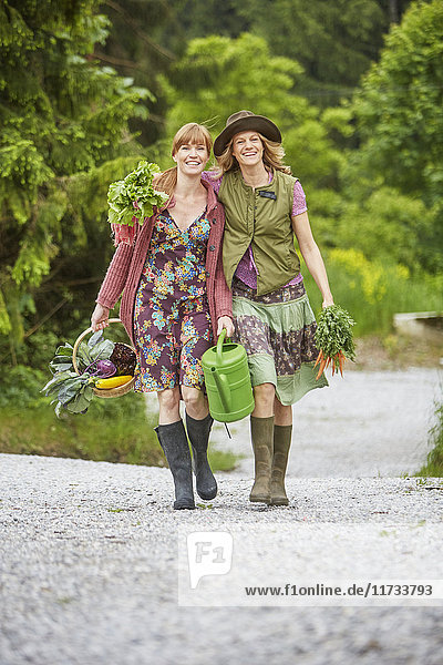 Two women carrying vegetables along rural road