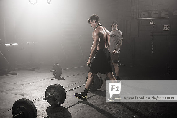Mid adult man about to lift barbell  while trainer looks on