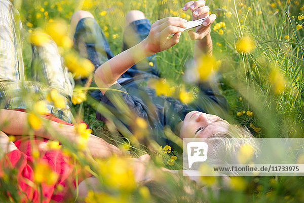 Im hohen Gras liegende Jungen spielen auf Smartphone