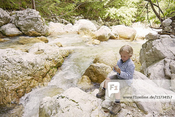 Boy sitting on rocks by woodland river  Bovec  Soca  Slovenia