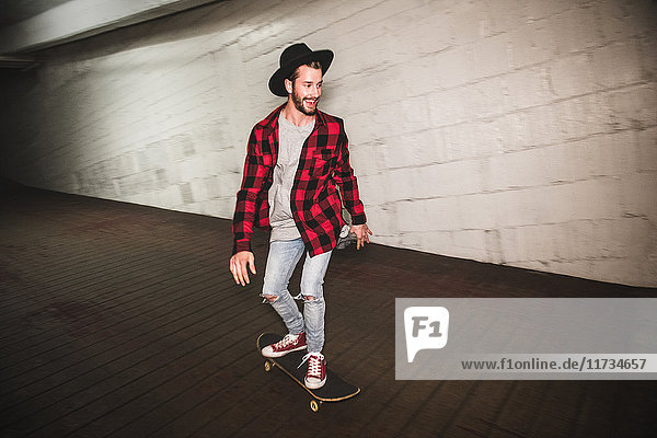 Male hipster skateboarding down sidewalk at night