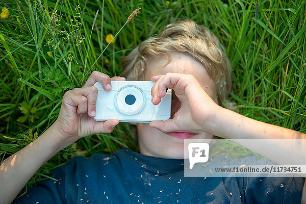 Junge liegt im Gras und fotografiert mit Smartphone