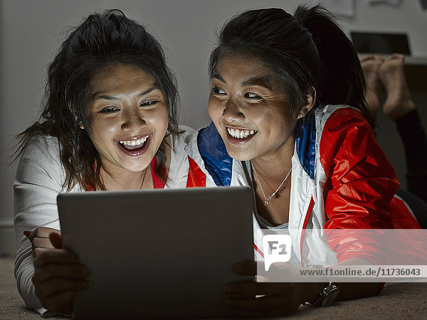 Two young women lying on floor looking at digital tablet