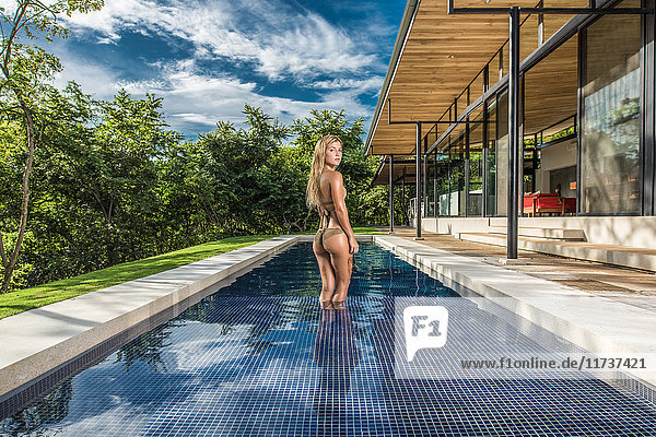 Portrait of young woman wearing gold bikini in holiday apartment swimming pool