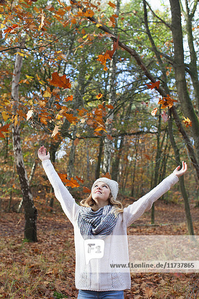 Teenager-Mädchen in Waldarmen erhoben  wirft Herbstblätter und schaut lächelnd auf