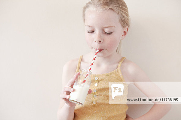 Young girl drinking glass of milk through straw