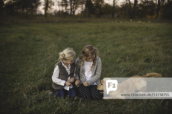 Zwei junge Mädchen sitzen mit ihrem Hund auf dem Feld