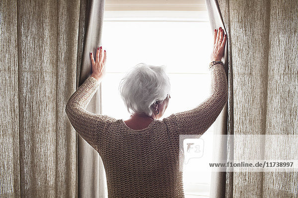 Senior woman opening curtains rear view