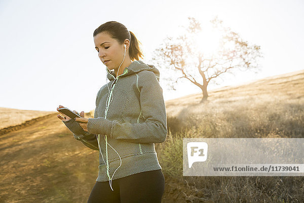 Female runner on sunlit hill choosing smartphone music