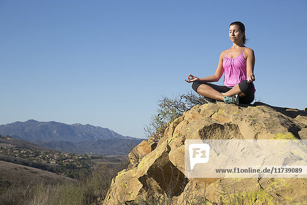Mature woman practicing yoga lotus pose on hill  Thousand Oaks  California  USA