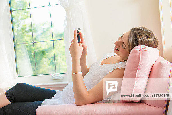 Schwangere  die auf einem Sessel sitzt und ein Smartphone benutzt