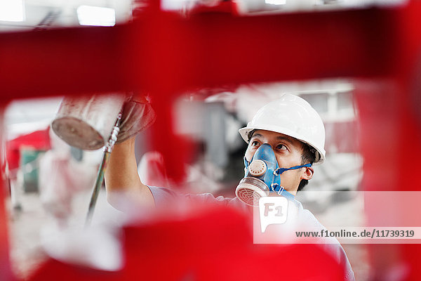 Nahaufnahme eines männlichen Fabrikarbeiters der einen roten Kran in einer Fabrikhalle besprüht China