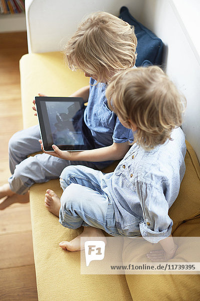 Zwei kleine Jungen sitzen auf einem Sofa und schauen auf ein digitales Tablet
