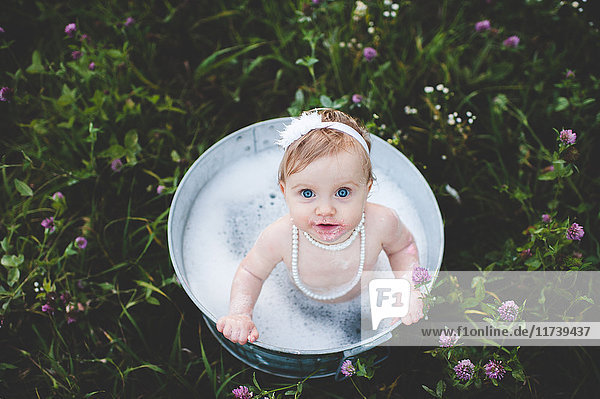 Draufsicht auf ein kleines Mädchen  das in einer Blechbadewanne in einer Wildblumenwiese badet