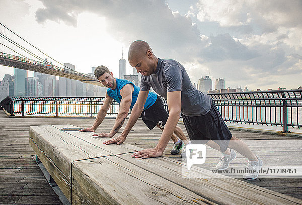Zwei junge Männer trainieren auf einer Bank am Flussufer  Brooklyn  New York  USA
