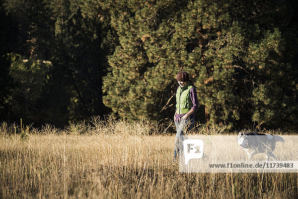 Mid adult woman walking dog in tall grass looking down smiling Missoula Montana USA