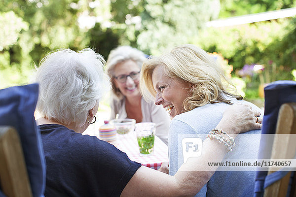 Drei Frauen entspannen sich gemeinsam im Garten und lachen
