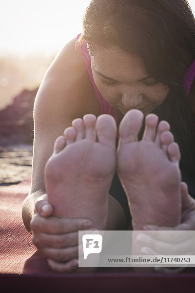 Nahaufnahme einer Frau  die im Morgengrauen ihre Füße hält und Yoga praktiziert
