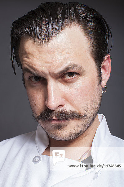 Close up studio portrait of mid adult male chef with raised eyebrow