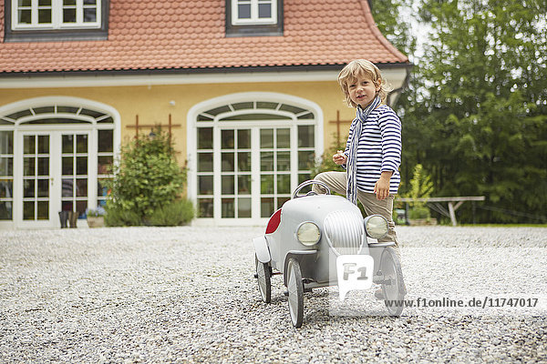 Junge spielt mit Oldtimer-Spielzeugauto vor dem Haus