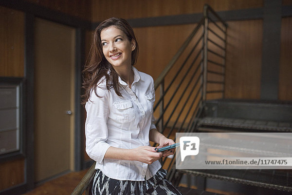 Young woman standing by metal staircase holding digital tablet