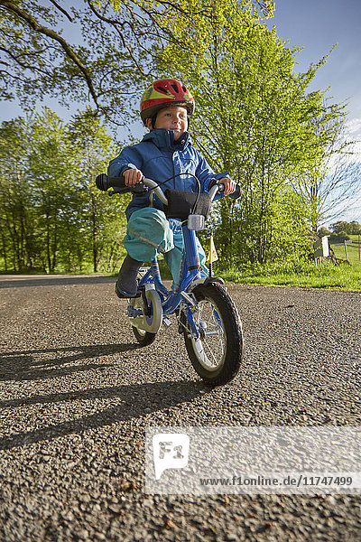 Junge mit rotem Fahrradhelm fährt auf Landstraße