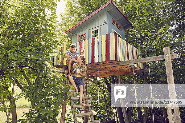 Junges Paar sitzt auf der Leiter eines Baumhauses