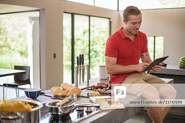 Mittelgroßer erwachsener Mann benutzt Digitaltechnik bei der Zubereitung von Speisen in der Küche