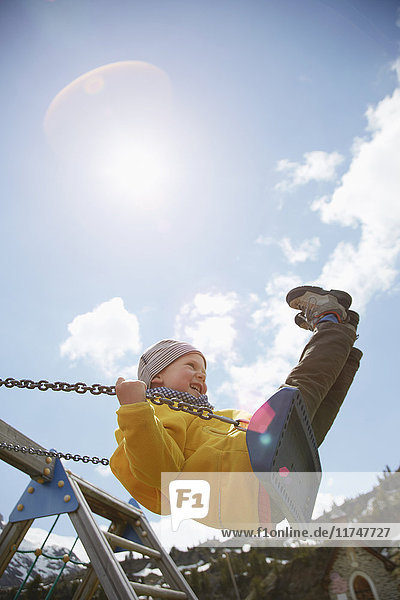 Young boy swinging high on playground swing
