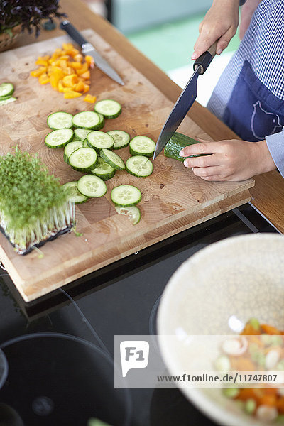 Woman slicing cucumber in kitchen