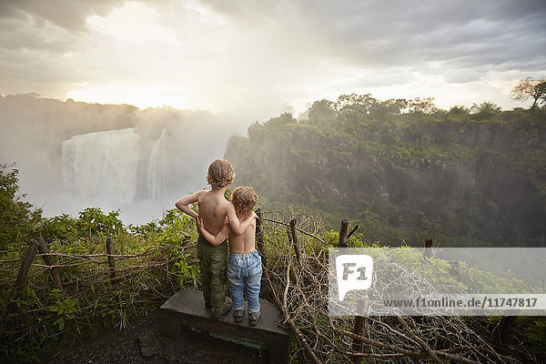 Two young boys standing on ledge admiring the view  rear view  Victoria Falls  Livingstone  Zimbabwe