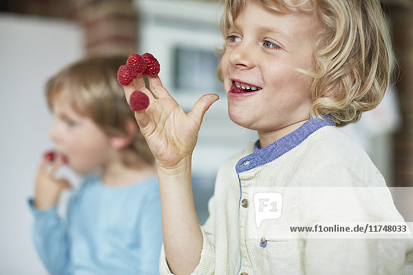 Two boys eating raspberries off fingertips