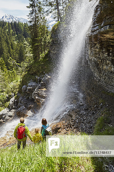 Junge Familie im Wald  stehend  Wasserfall beobachtend  Rückansicht