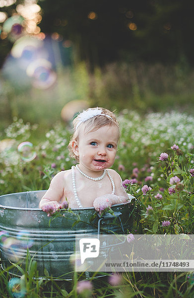 Porträt eines Mädchens  das in einer Blechbadewanne auf einer Wildblumenwiese badet