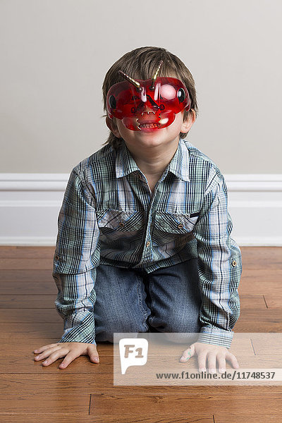 Porträt eines Jungen  auf dem Boden kniend  mit Maske